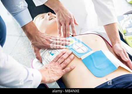 First-aider placing automated external defibrillator (AED) pads on a CPR training dummy. Stock Photo