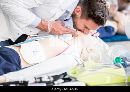 Doctor practising rescue breaths on a CPR training dummy. Stock Photo