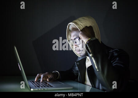 Concentrated young hacker using computer and stealing information in dark room Stock Photo