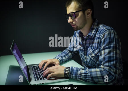 Young man working on computer at night in dark office. The designer works in the later time. A young man sits at the computer Stock Photo