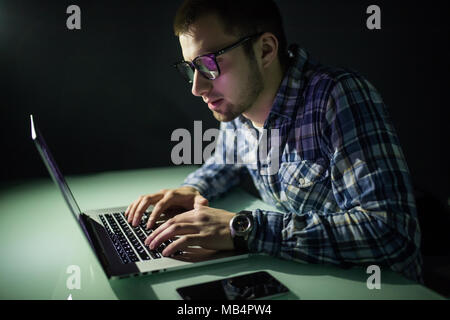Concentrated young hacker using computer and stealing information in dark room Stock Photo