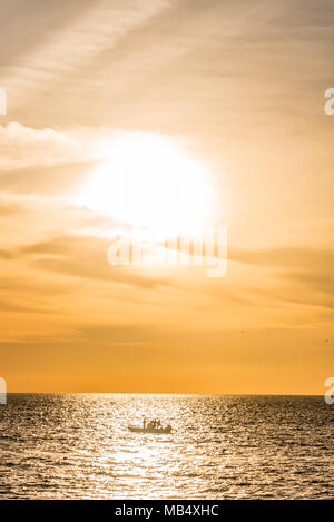 Colorful orange sunset over a tropical ocean with a lone small boat silhouetted in the reflection from the sun on the water Stock Photo