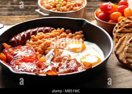 English Breakfast with sausages, grilled tomatoes, egg, bacon, beans and bread on frying pan. Stock Photo