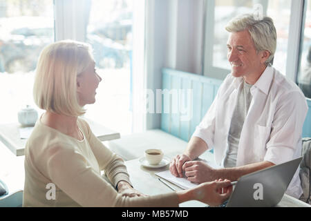 Two mature business partners discussing online financial statistics or new project in laptop at meeting in cafe Stock Photo