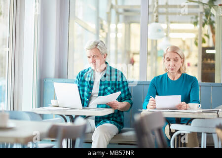 Senior businessman with contract making changes in its text in laptop while his colleague checking data in financial papers near by Stock Photo