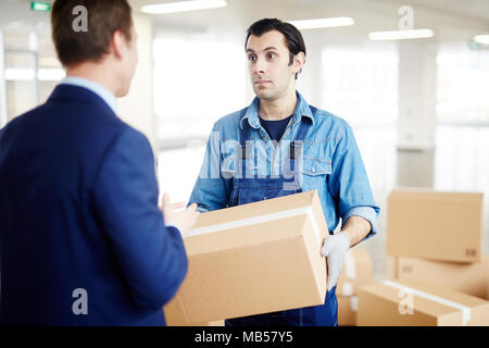 Gloved worker in uniform talking to businessman about where to remove boxes with office supplies Stock Photo
