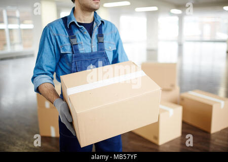 Gloved worker in uniform carrying packed box with supplies while doing his work during relocation Stock Photo