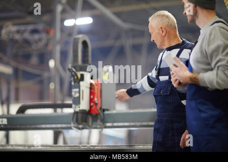 Two professionals in workwear discussing engine system of new boat during work in factory Stock Photo