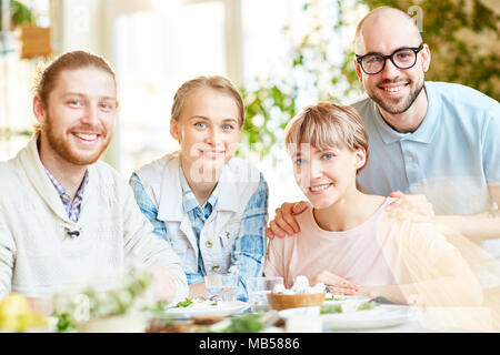 Happy girls and guys enjoying dinner at weekend while spending time in cafe Stock Photo