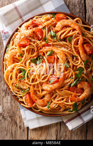 Italian pasta spaghetti with prawns, parmesan and herbs in tomato diavolo sauce close-up on a plate. Vertical top view from above Stock Photo