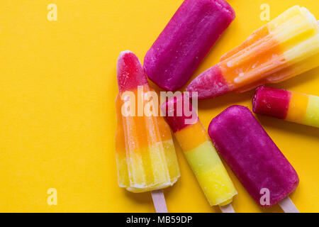 A selection of bright summer ice lollies on a yellow background Stock Photo