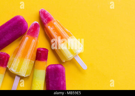 A selection of bright summer ice lollies on a yellow background Stock Photo