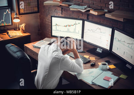 Young bearded man trader at office sitting at table holding head exhausted top view hard-working Stock Photo