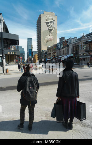Pedestrians waiting to cross the street, at the corner of de Maisonneuve and Crescent , Montreal. A huge mural of the late  Leonard Cohen is visible. Stock Photo