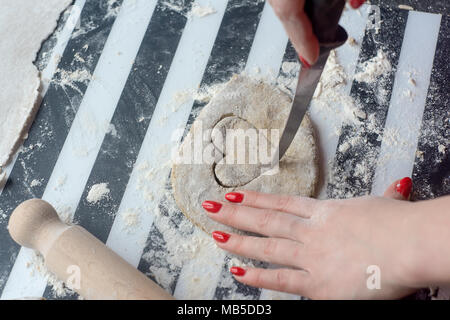 Woman carved heart from dough for cookies, she have nice red nails. Stock Photo