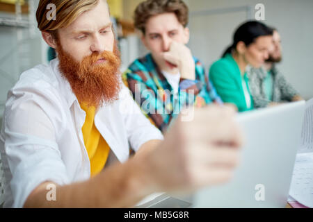 Concentrated businessman using laptop. He is sitting together with his colleagues at the table Stock Photo