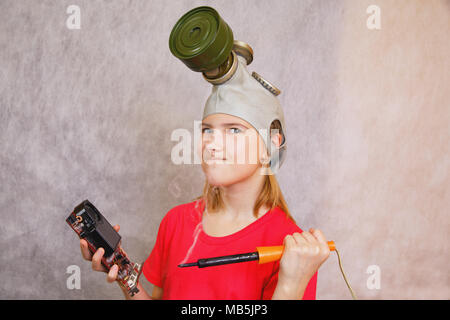 Comic, distortion: girl teenager wearing a gas mask, is preparing to pierce, destroy a hot soldering iron non-working electronic card Stock Photo