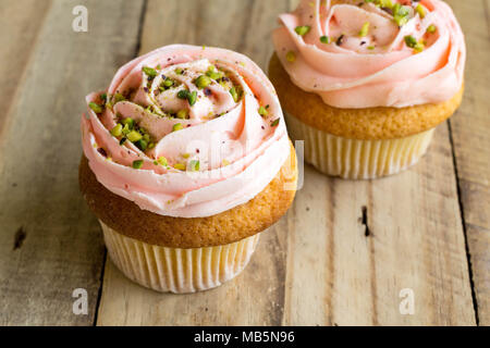 Two pink cup cakes with pistachio nut sprinkles and candles on black ...