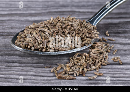 Close-up of aromatic caraways on wood. Carum carvi. Pile of dried cumin seeds on stainless spoon partially spilled on harmonic brown-toned background. Stock Photo