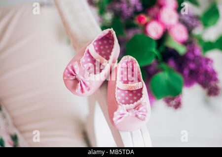 Closeup top view of pair of small sweet new pink shoes for little infant on sofa in home interior. Blurry colorful flowers in background. Happy expect Stock Photo