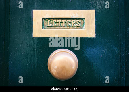 Old brass mail letter box and door knob on a green front door, text letters Stock Photo