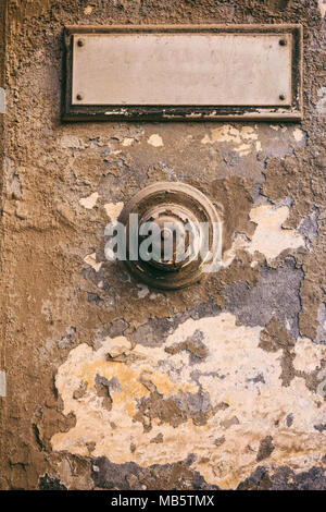 Weathered door bell and blank name label on damaged wall background Stock Photo