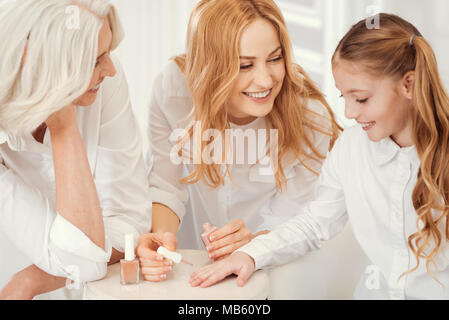 Tender granny and mom teaching child hot to paint nails Stock Photo