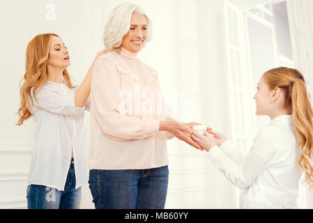 Loving daughter and grandchild helping their granny with dressing up Stock Photo