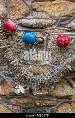 An artwork on a stone wall of a cottage in st Ives in Cornwall made from flotsam and jetsam with fishing nets and floats in a nautical or maritime way Stock Photo