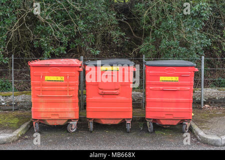Three large size red wheelie bins / wheely bins / rubbish bins. Metaphor for waste disposal, refuse disposal, rubbish, trash, redundant data metaphor. Stock Photo