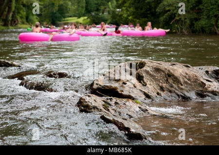 A Group Of Defocused People Tubing Down River Approach Boulders In Focus Stock Photo