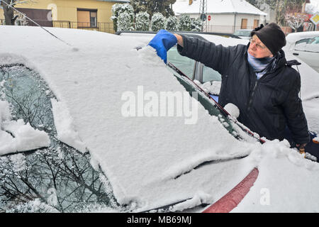 Driver cleaning snow from the windshield of a car using a brush. Stock Photo