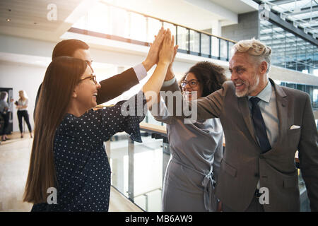 Smiling and laughing business team giving high five to each other during teambuilding in office. Stock Photo