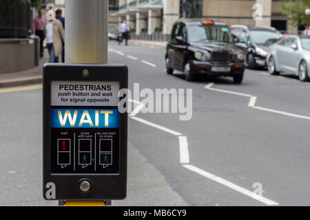 Illuminated 'Wait' pedestrian sign at a pedestrian crossing on a busy road in central London, England Stock Photo