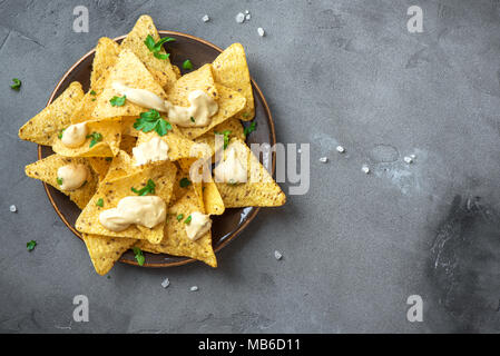 Nachos chips and melted cheese. Tortilla corn mexican nachos chips in bowl and cheese sauce dip on grey stone background, copy space. Stock Photo
