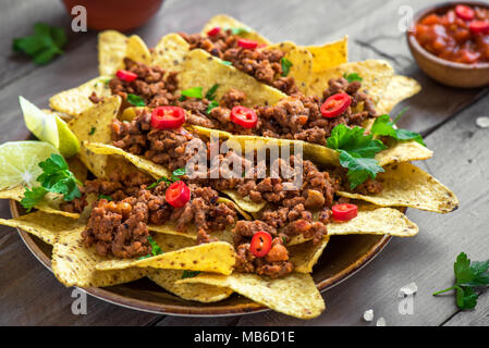 Mexican nacho corn tortilla chips with  meat and red hot spicy salsa. Nachos with ground beef on wooden background. Stock Photo
