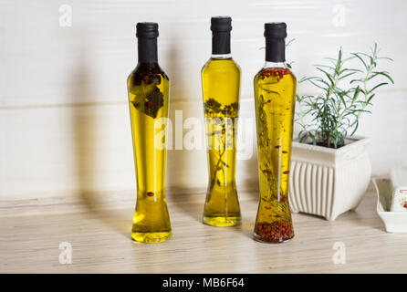 Three bottes of  olive oil with spieces, rosemary, pepper, oregano, allspice, bay leaf and pot with rosemary  on the kitchen table Stock Photo