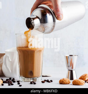 pour the frappe from the shaker into a tall glass , beautiful and clean composition with coffee beans and amaretti biscuits Stock Photo