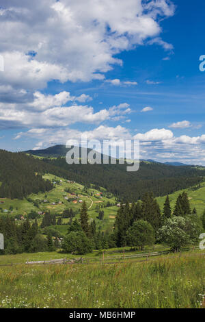 Amazing view of beautiful cloudy summer landscape and village in distance. Tops of mountains and old thick wood growing on hills. Vertical color image Stock Photo