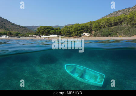 Spain coastline Cala Montjoi beach on the Costa Brava and a small boat wreck underwater, split view above and below water surface, Mediterranean sea Stock Photo