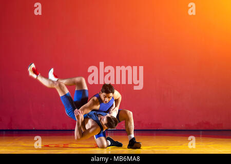 Two strong wrestlers in blue  wrestling tights are wrestlng and making a  making a hip throw  on a yellow wrestling carpet in the gym. Young man doing Stock Photo