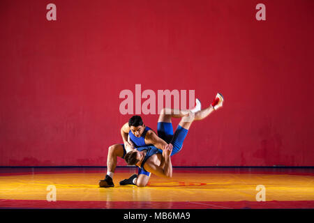 Two strong wrestlers in blue  wrestling tights are wrestlng and making a  making a hip throw  on a yellow wrestling carpet in the gym. Young man doing Stock Photo