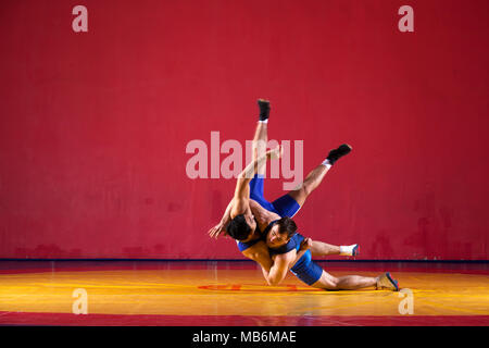 Two strong wrestlers in blue wrestling tights are wrestlng and making a suplex wrestling on a yellow wrestling carpet in the gym. Young man doing grap Stock Photo