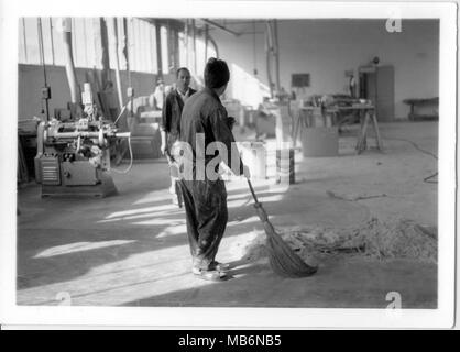 Young man cleaning an old 1970s factory with his boss cheking his work. Old job.  Italy Stock Photo