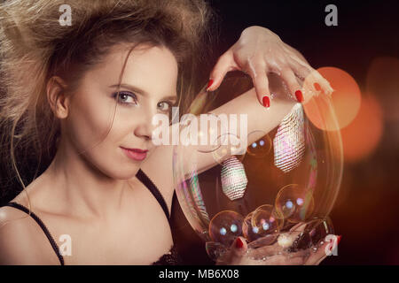 girl plays with big soap bubbles on black background with lights Stock Photo