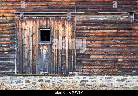 Side of Barn showing Distressed Board Door with Window and Stone Wall Foundation. Stock Photo