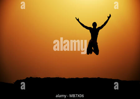 Silhouette of a young man jumping with arms stretched out Stock Photo
