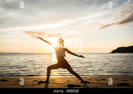 Silhouette of a fit woman practicing the warrior yoga pose at sunset Stock Photo