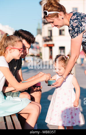 Family spending time together in the city centre enjoy eating ice cream on summer day. Mother, toddler and teenage girl and boy spending quality time Stock Photo