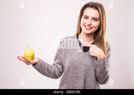 Portrait of a smiling pretty girl holding an apple and pointing finger isolated over white Stock Photo